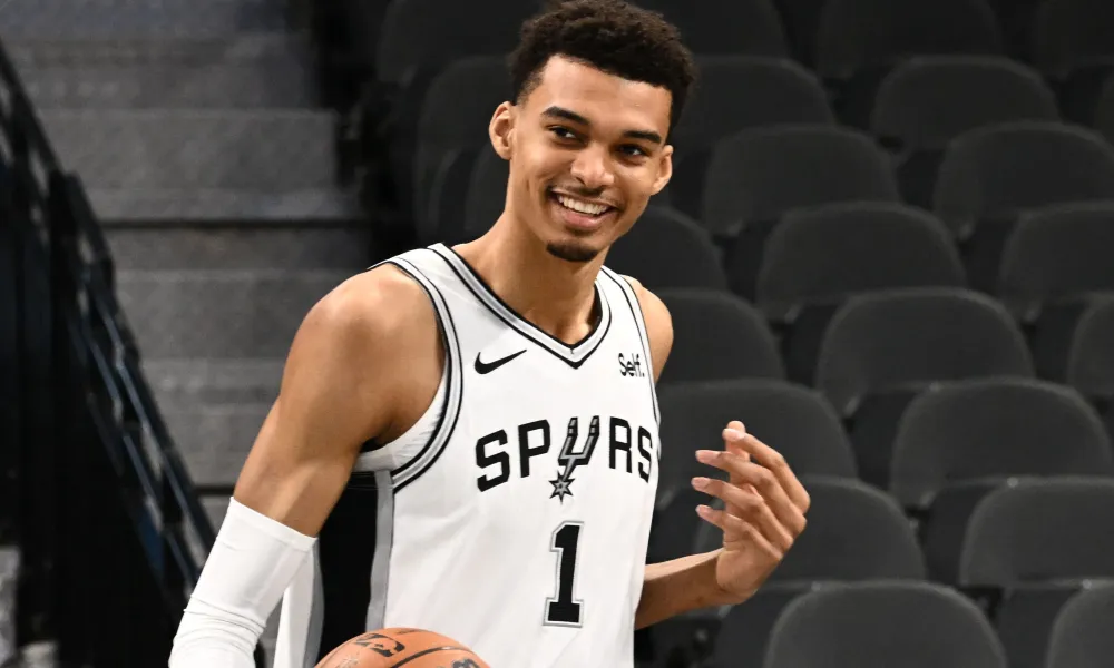 A basketball player from the Spurs team smiles as he holds a basketball.